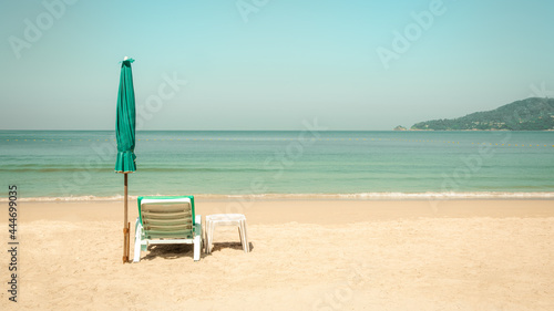 Fototapeta Naklejka Na Ścianę i Meble -  White plastic beach chair, table and green umbrella on tropical sand beach by the sea in summer of Phuket, Thailand in pastel color tone. 