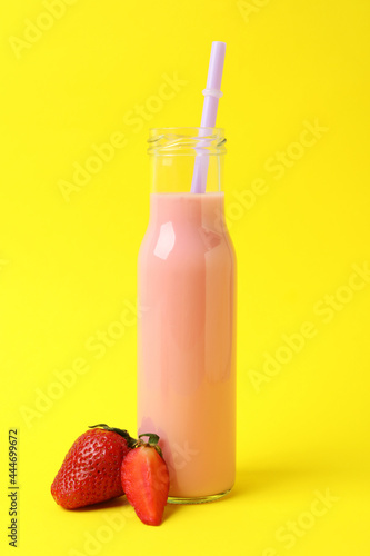 Glass bottle of strawberry milkshake on yellow background