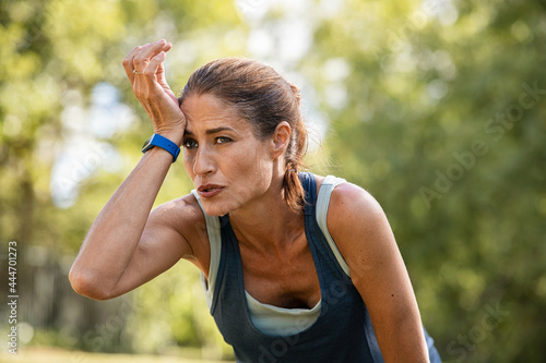 Foto Tired mature runner wiping sweat after workout at park