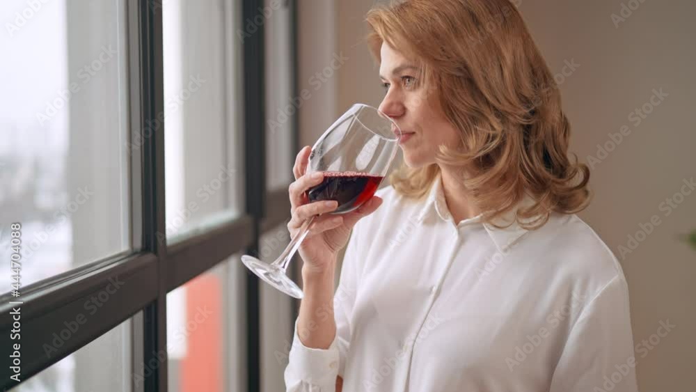 side view elegant middle aged woman in white shirt standing near window drinking red wine time for break and relax side view elegant middle aged woman in white shirt standing near window drinking red wine time for break and relax