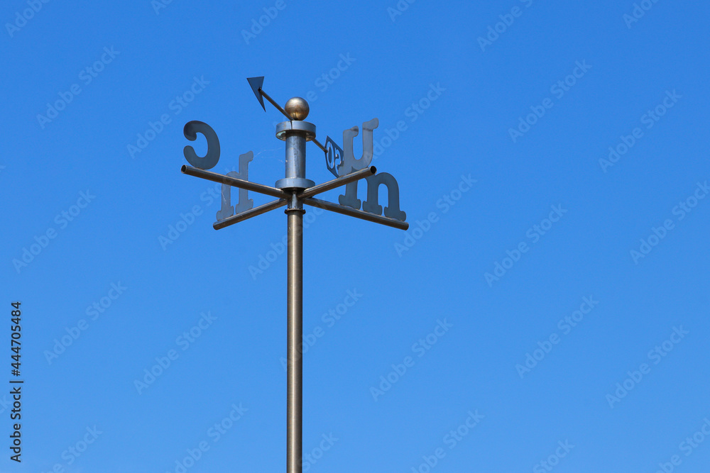 A  weather vane with Welsh letters for the direction against a clear blue sky