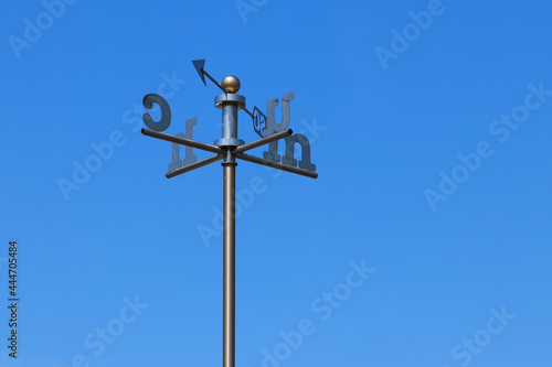 A weather vane with Welsh letters for the direction against a clear blue sky