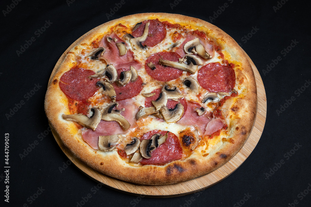 Pizza with tomato sauce, mozzarella, salami and mushrooms on a black background.