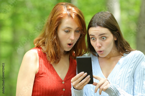 Foto Amazed women checking surprising phone content in a park