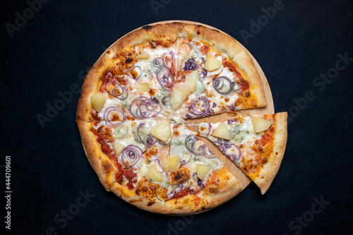 Pizza with tomato sauce, mozzarella, gorgonzola cheese, red onion and pineapple on a black background.