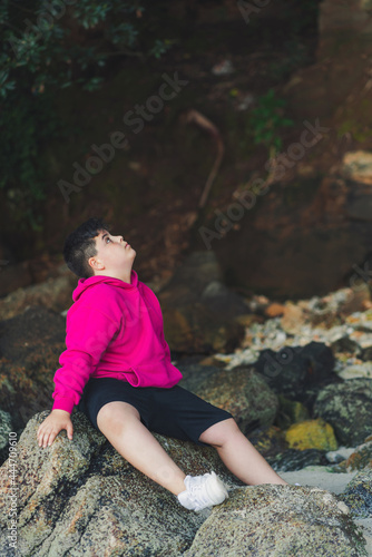 Ni  o sentado en la roca en una playa escondida de Galicia