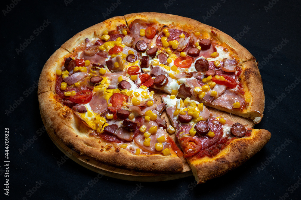 Pizza with tomato sauce, mozzarella, sour cream, salami, pork ham, sausages, corn and cherry tomatoes on a black background