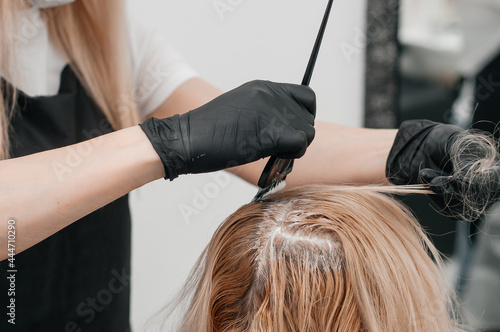 Girl in a beauty salon. A craftsman in black gloves smears paint on the hairs. hair dyeing services.