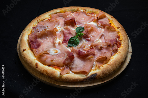 Pizza with tomato sauce, mozzarella and ham on a black background.