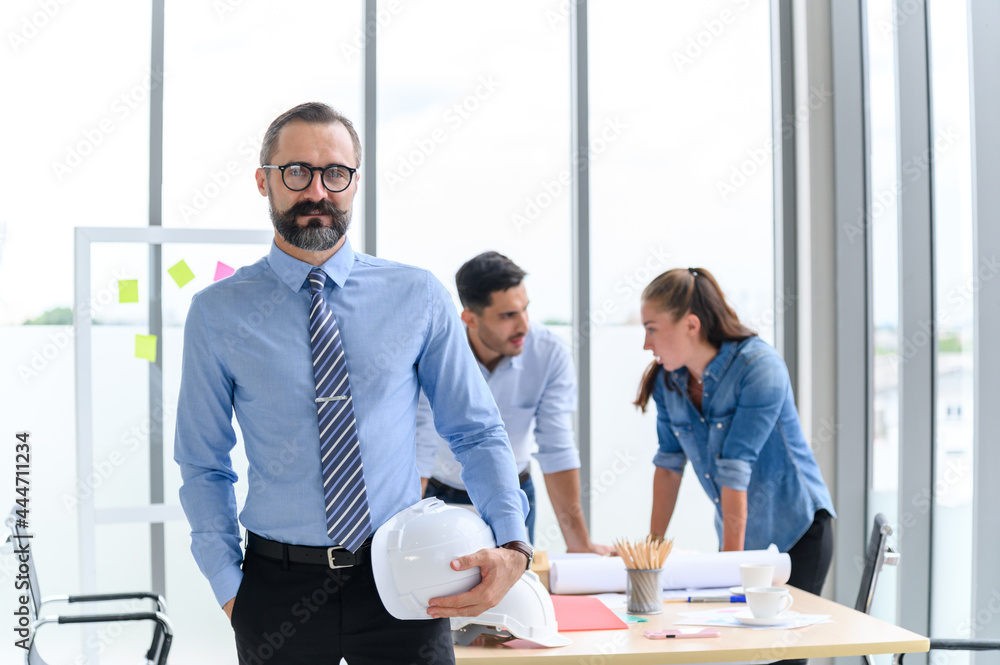 construction engineer manager stand and holding white hardhat in front of engineers team meeting for architectural project in the office construction site construction engineer manager stand and holding white hardhat in front of engineers team meeting for architectural project in the office construction site