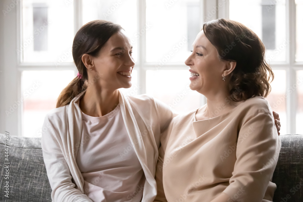 Happy millennial girl and old Caucasian mom sit rest on sofa at home talk chat on family weekend. Smiling adult grownup daughter and middle-aged mother relax in living room have close bonding time. Happy millennial girl and old Caucasian mom sit rest on sofa at home talk chat on family weekend. Smiling adult grownup daughter and middle-aged mother relax in living room have close bonding time.