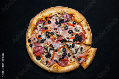 Pizza with tomato sauce, salami, pork ham, olives, peppers and mushrooms on a black background.