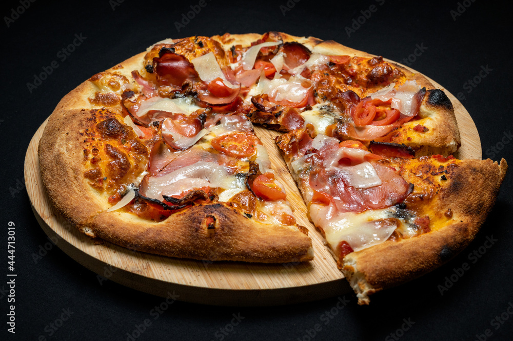 Pizza with tomato sauce, smoked pork ham, mozzarella and cherry tomatoes on black fudal