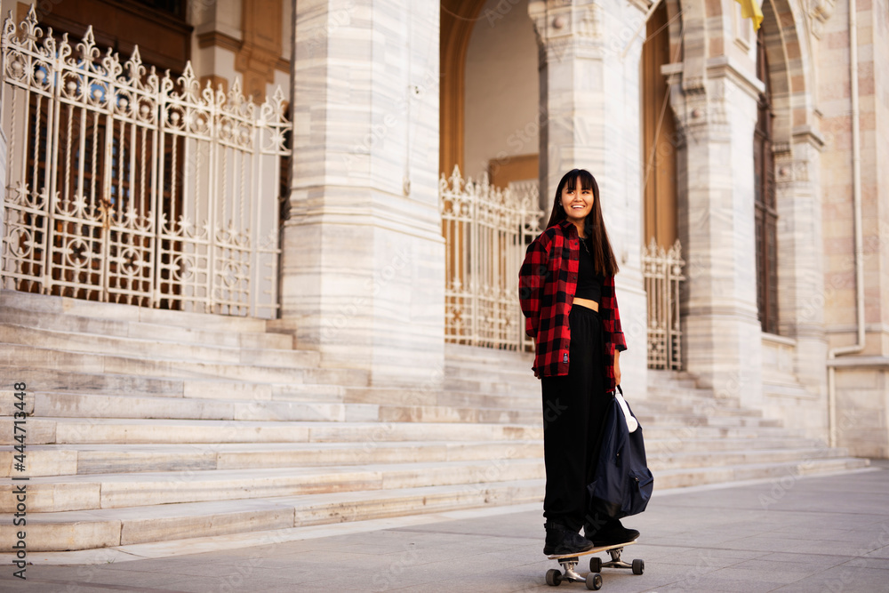 Fototapeta premium Portrait of young beautiful girl with skateboard. Happy smiling woman relaxing outdoors.