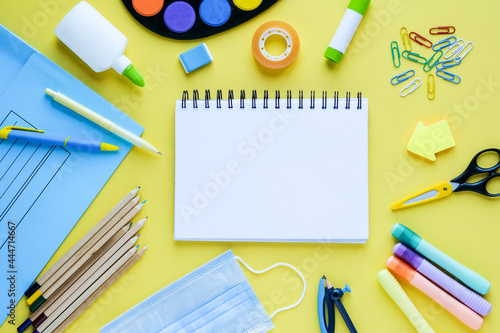Back to school with school supplies, stationery, medical mask and notebook with empty blank space for kids on yellow desk background,top view flat lay..