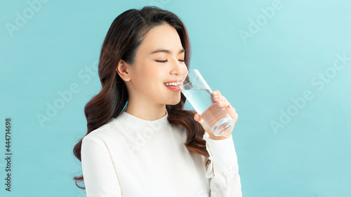 Young woman drinking water on blue background
