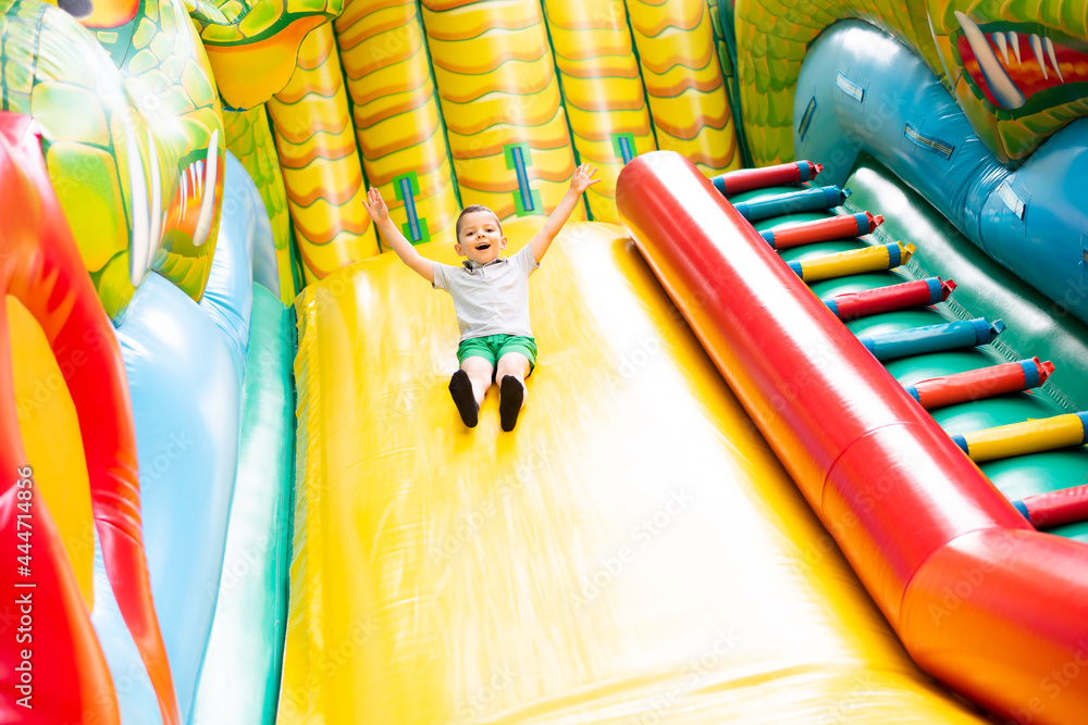 Little boy child rides on an inflatable multi-colored slide. - obrazy, fototapety, plakaty 