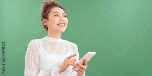 Fotografie Photo of cheerful cute beautiful young woman chatting by mobile phone isolated over green wall background