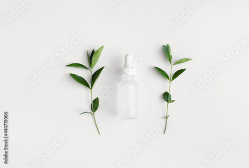 Cosmetic glass bottle with pipette  green leaves on white background. Skincare beauty product. Flat lay  top view.