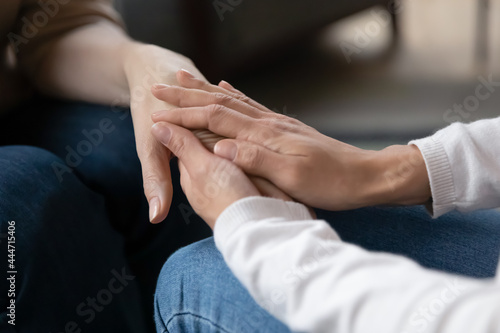 Crop close up of caring girl child hold unhappy old mother hands show love and support in difficult situation. Supportive daughter comfort caress mature mom feel grateful thankful. Gratitude concept.