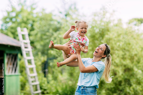 A young mother and her cute little girl are having fun in a sunny garden. The concept of a happy childhood and motherhood  a mother holds her little daughter in her arms