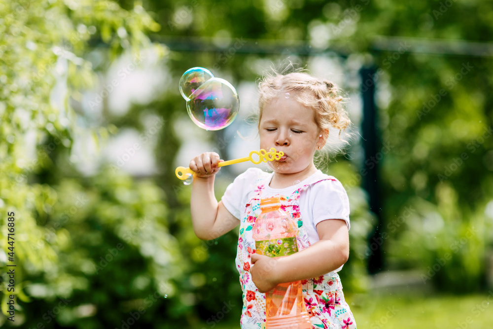 A little girl blows soap bubbles in the park. Happy childhood, summer time. Side view