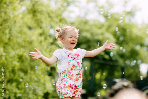 A cheerful girl catches soap bubbles with her hands and laughs. Happy childhood  summer time