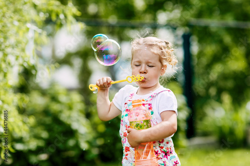 A little girl blows soap bubbles in the park. Happy childhood, summer time. Side view
