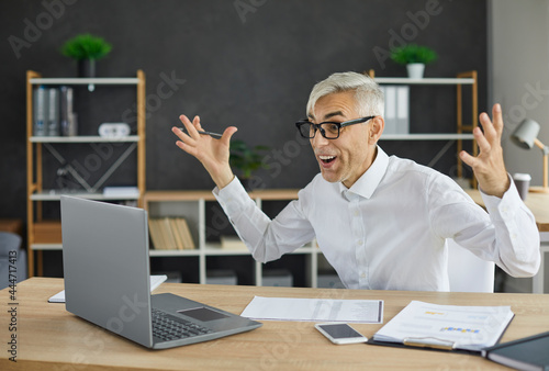 Obraz na płótnie Mature businessman sitting with hands raised at office table and looking at scre
