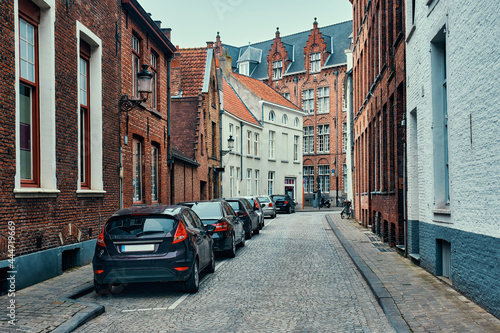 Brugge street with cobblestone road with parked cars and old medieval houses. Bruges, Belgium