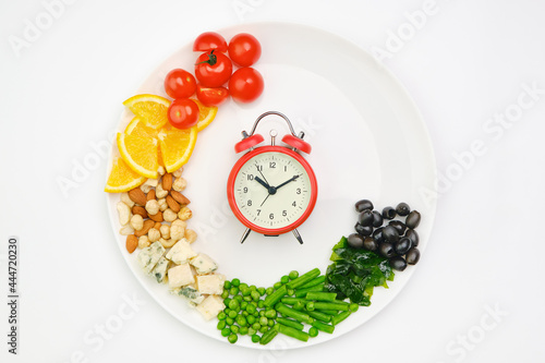 Diet and lunchtime, Intermittent fasting concept. Vegetables, oranges, cheese, nuts and clock on a white plate. Healthy dietary food. photo