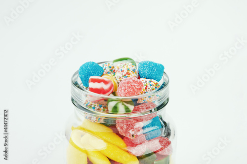 Assorted candies in a glass jar on a white background.