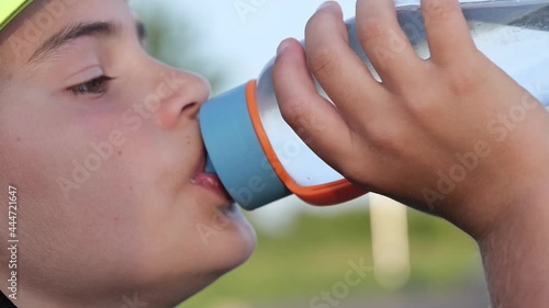 Cute teenager child kid in helmet drinking water from sport bottle outdoor in park