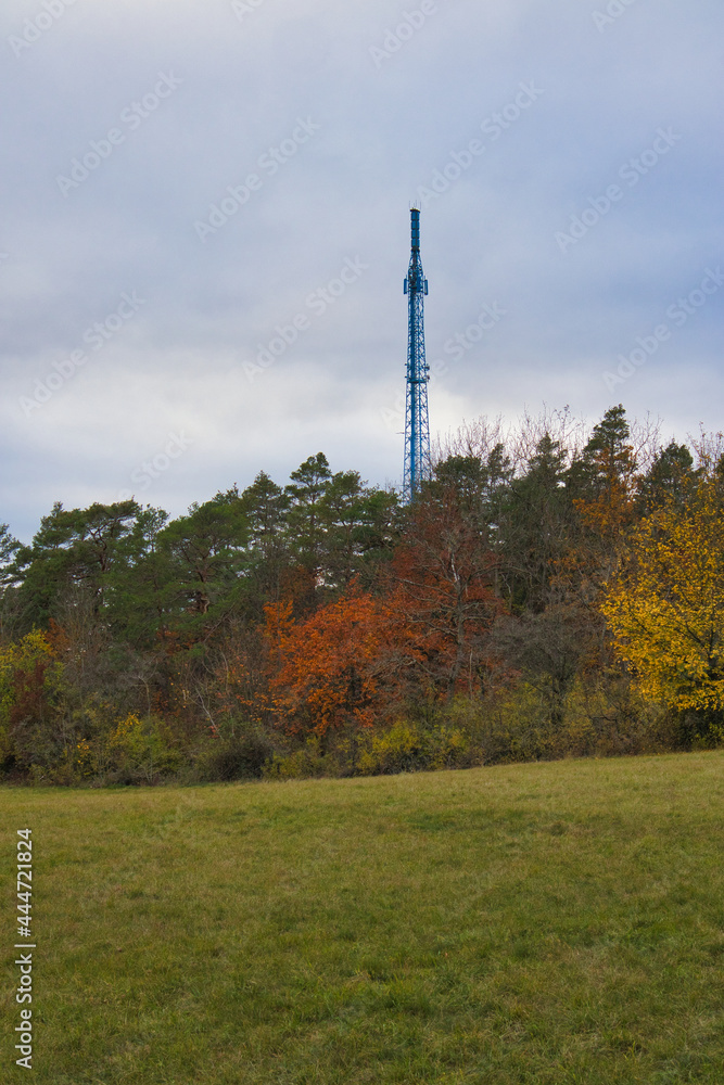 Obraz premium Blauer Funkturm auf dem Landgrafen hinter herbstlichem Mischwald und grüner Wiese, Jena, Thüringen, Deutschland