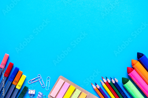 School office supplies lie from below on light blue background. Colorful pencils, felt-tip pens, brushes, stickers and stationery flat lay. Back to school and new academic year concept. Copy space
