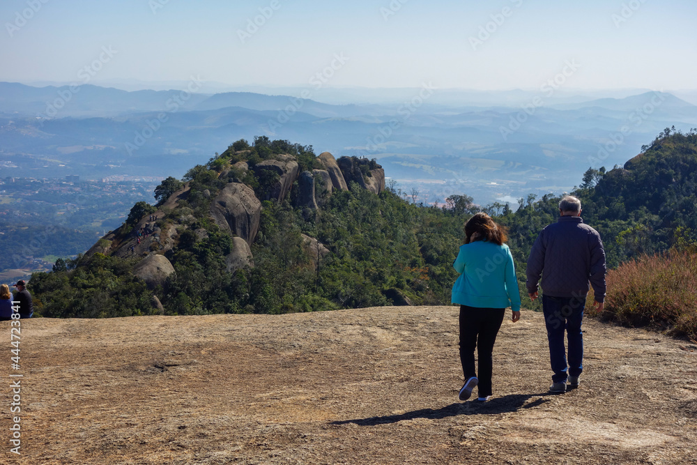 couple walking over a huge stone of natural monument on the highs, with mountainscape on background