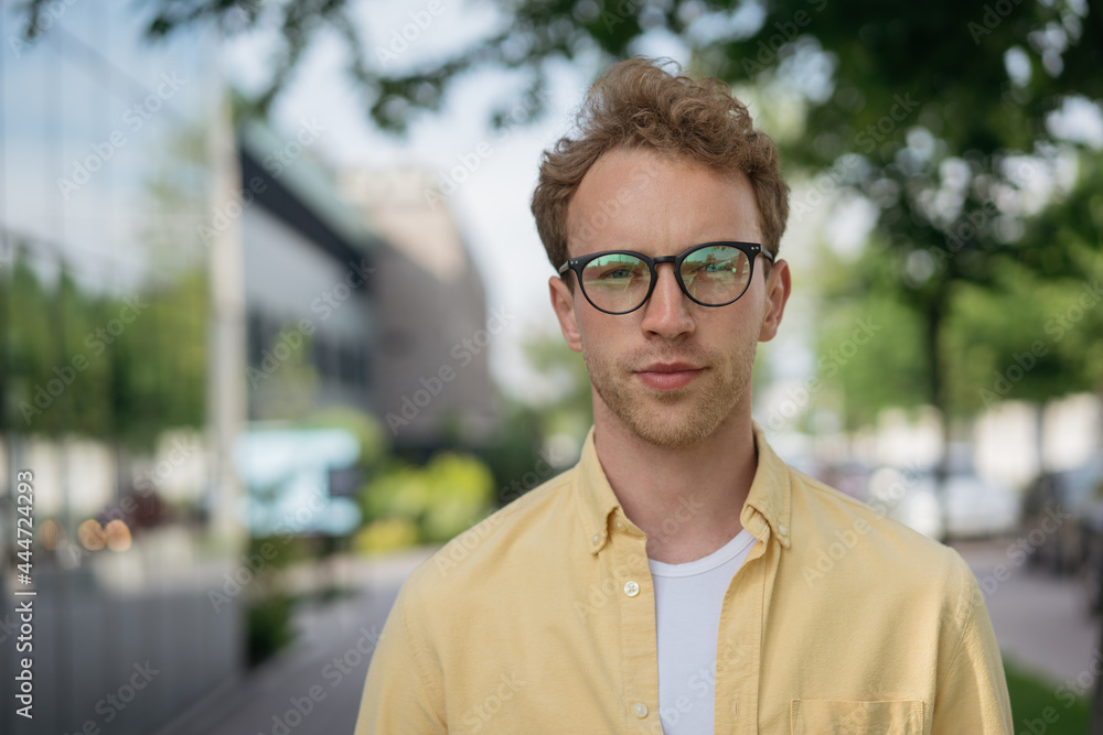 Young confident businessman wearing yellow shirt and stylish eyeglasses looking at camera on the street, copy space. Successful business. Portrait of pensive university student, education concept Young confident businessman wearing yellow shirt and stylish eyeglasses looking at camera on the street, copy space. Successful business. Portrait of pensive university student, education concept
