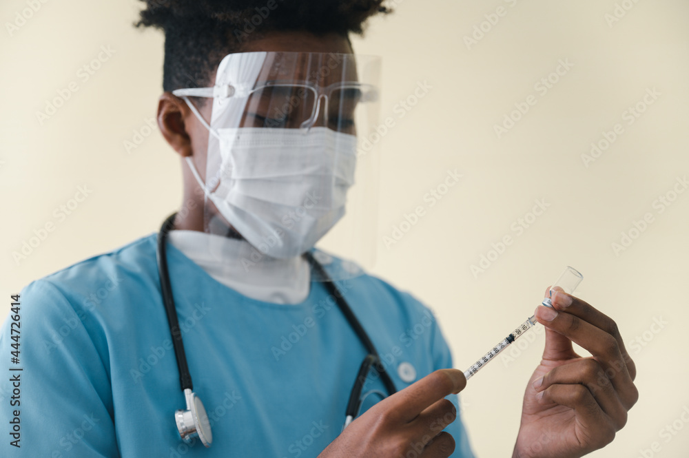 African-American man doctor wearing a mask and face shield. Holding a syringe with a bottle of coronavirus19 vaccine protection in a laboratory. Concept of protection against the COVID-19 virus. African-American man doctor wearing a mask and face shield. Holding a syringe with a bottle of coronavirus19 vaccine protection in a laboratory. Concept of protection against the COVID-19 virus.