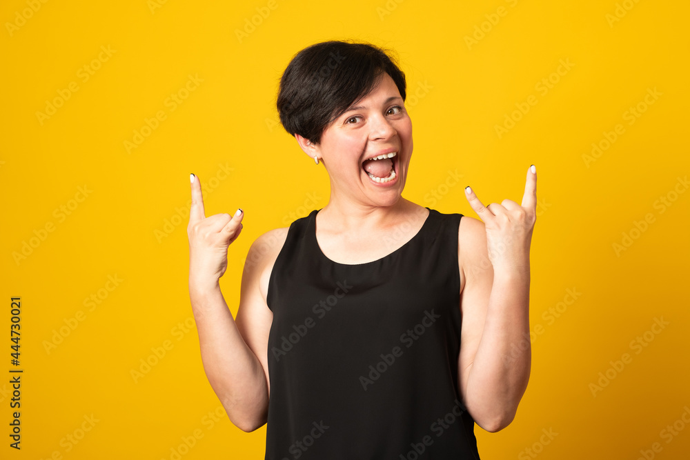 Emotive woman makes rock n roll sign, says I will rock this party, yells loudly, casual t shirt, stands over yellow background, feels self confident. Emotive woman makes rock n roll sign, says I will rock this party, yells loudly, casual t shirt, stands over yellow background, feels self confident.
