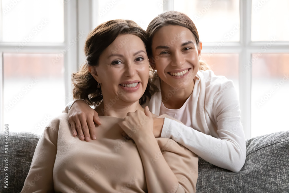 Portrait of happy young millennial girl child hug middle-aged Caucasian mother relax together at home. Smiling adult grownup daughter and mature mom embrace show love and care in family relations. Portrait of happy young millennial girl child hug middle-aged Caucasian mother relax together at home. Smiling adult grownup daughter and mature mom embrace show love and care in family relations.
