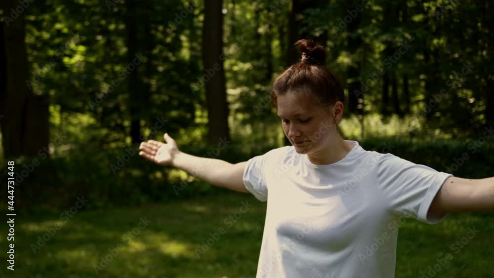 Woman white t-shirt goes sports public park forest early morning. Stretches arms body stretches before training. Yoga balance, take care your health, tone body, muscles, balance nature, slow movements Woman white t-shirt goes sports public park forest early morning. Stretches arms body stretches before training. Yoga balance, take care your health, tone body, muscles, balance nature, slow movements