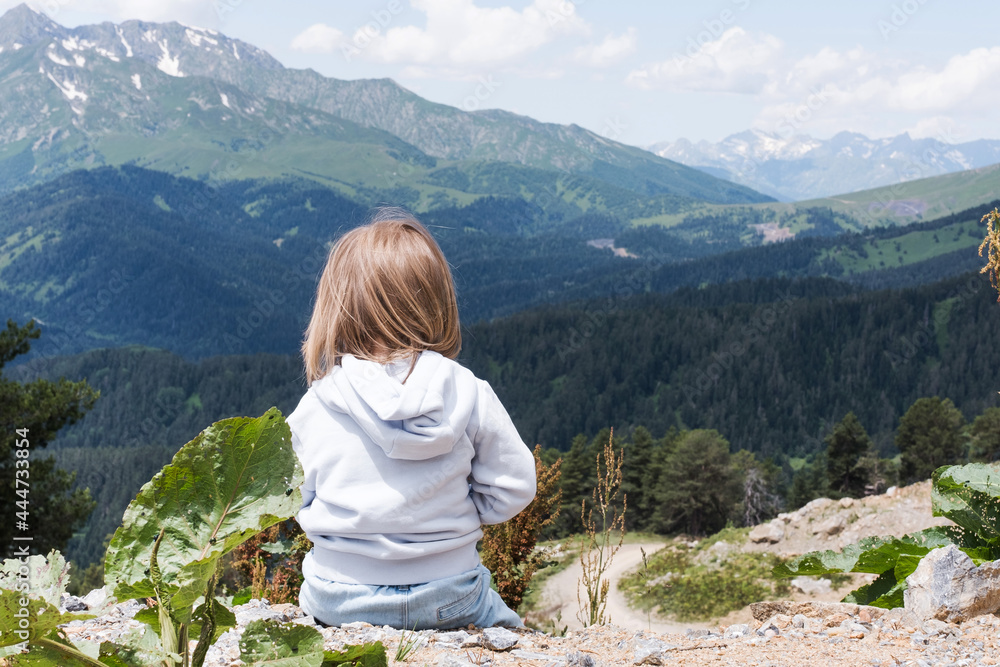 The child is sitting and looking at the landscape of the Caucasus Mountains. Outdoor travel, local travel.