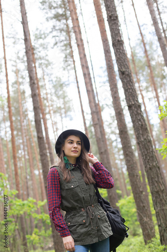 Young woman in a hat with  her backpack walking while traveling in forest and exploring local nature © mariarom