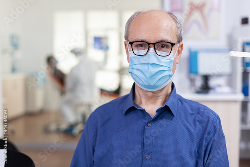 Portrait of elderly man in dental office looking on camera wearing face mask sitting on chair in waiting room stomatological clinic. Concept of new normal dentist visit in coronavirus outbreak. © DC Studio