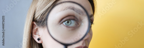 Young woman holding magnifying glass in front of her eye closeup