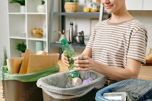 Young female smashing plastic bottle over one of three trash bins photo