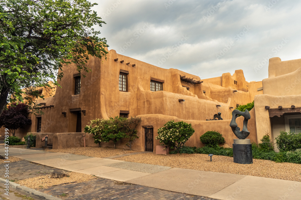 Naklejka premium Pueblo Revival Style building with earth tone color, rounded corners and battered walls under dramatic cloudy sky, side, New Mexico Museum of Art, Santa Fe, New Mexico