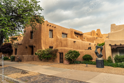Pueblo Revival Style building with earth tone color, rounded corners and battered walls under dramatic cloudy sky, side, New Mexico Museum of Art, Santa Fe, New Mexico photo