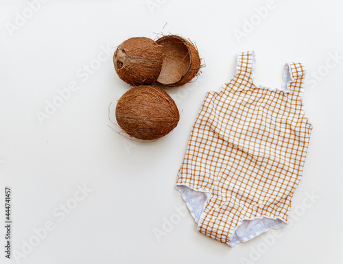 Baby swimsuit and coconut on beige aground, minimal summer holiday composition flat lay photo