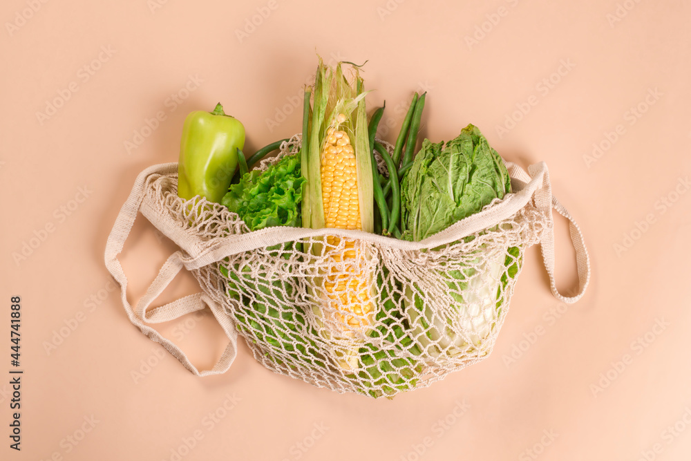 Mesh string bag with green vegetables and herbs on a beige background. Sustainable lifestyle. Eco-friendly concept.